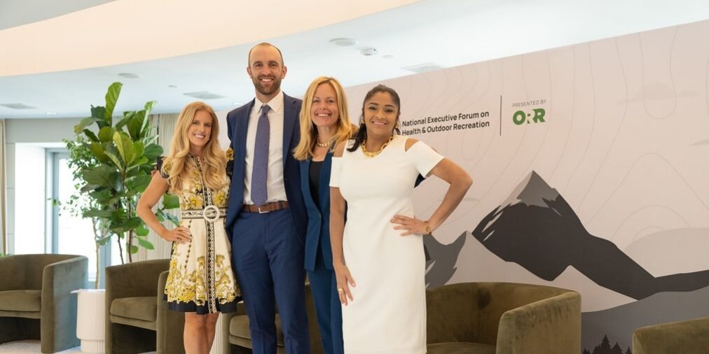 ORR_Team_Photo Three women and one man stand on a stage in business professional attire. The backdrop reads, "ORR."