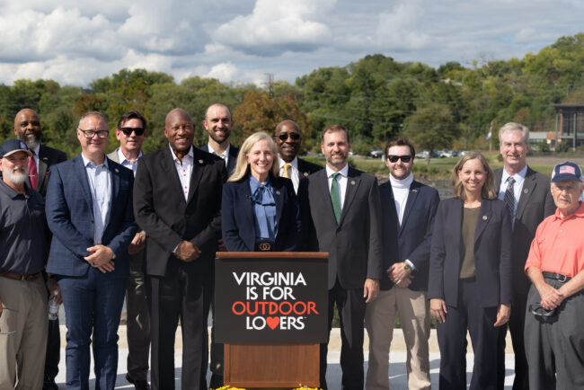 Governor Spanberger and eleven professionals outside, around a podium that reads "Virginia is for Outdoor Lovers."