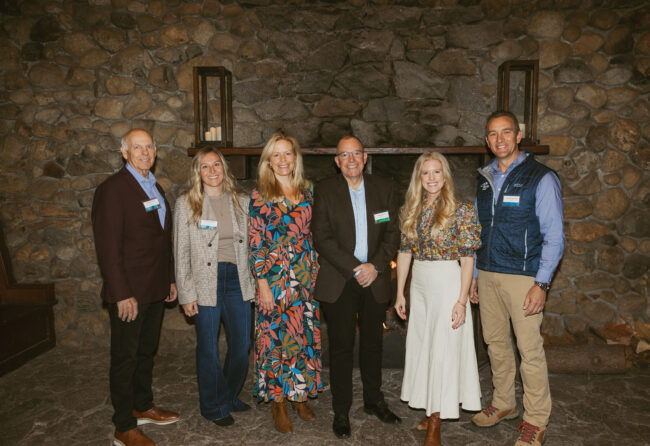 Six professionals, including members of the Administration, stand in front of a fire place in Valhalla Tahoe.